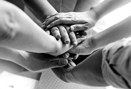 Photo noir et blanc de 7 mains empilées les unes sur les autres, solidarité